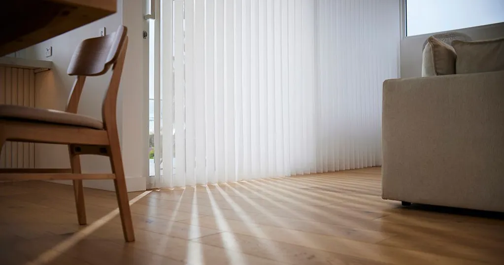 SmartDrape sheer vertical vanes filtering sunlight across a timber floor in a dining and living space